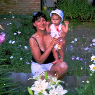 Woman and baby playing in shallow water surrounded by flowers.