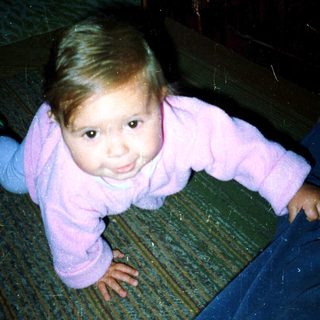 Young child crawling indoors, wearing pink onesie.