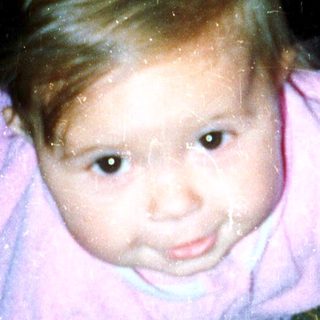 Young child crawling indoors, wearing pink onesie.