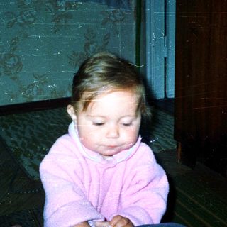Young child sitting indoors, wearing pink clothing.