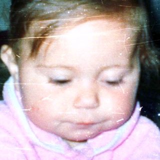 Young child sitting indoors, wearing pink clothing.