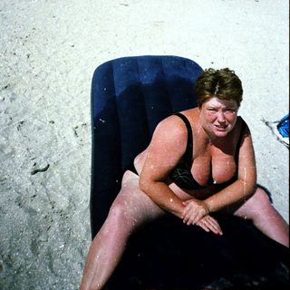 Person sitting on inflatable in sandy outdoor area.