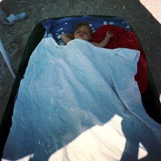 Baby sleeping peacefully in makeshift bed outdoors.