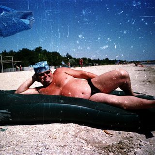 Man relaxing on inflatable tube under beach umbrella.