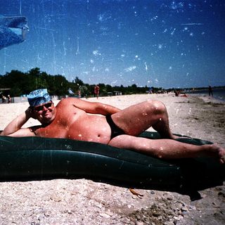 Man relaxing on inflatable tube under beach umbrella.