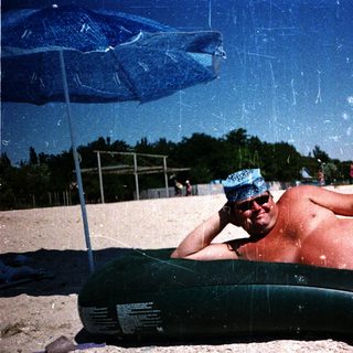 Man relaxing on inflatable tube under beach umbrella.