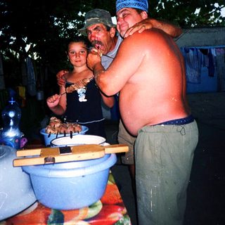 Family barbecuing outdoors under trees at night.