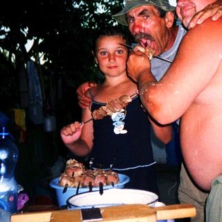 Family barbecuing outdoors under trees at night.