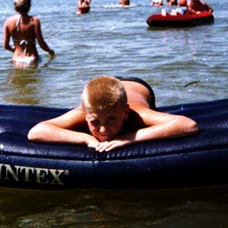 Person relaxing on inflatable float in crowded beach water.