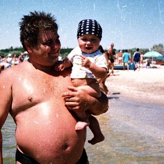 Man holding baby in shallow beach water.