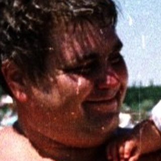 Man holding baby in shallow beach water.