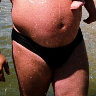 Man holding baby in shallow beach water.