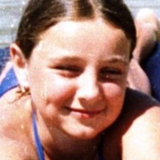 A child lying on an inflatable raft in shallow beach water.