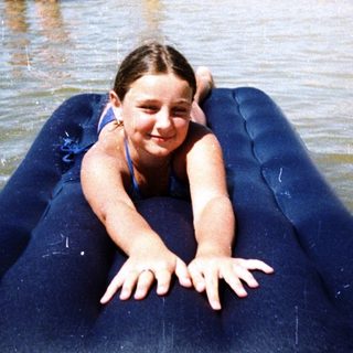 A child lying on an inflatable raft in shallow beach water.