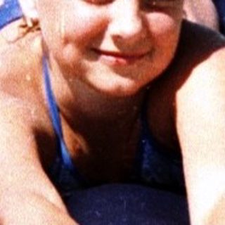 A child lying on an inflatable raft in shallow beach water.