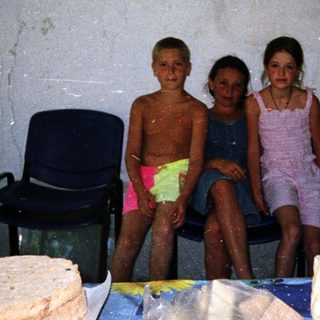 Three children posing indoors near food items.