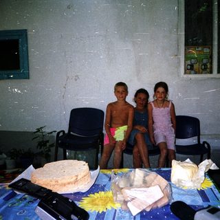Three children posing indoors near food items.