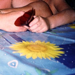 Shirtless man and boy sitting outdoors by water.