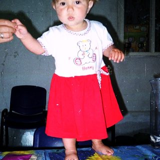 Toddler standing on table holding adult's hand.