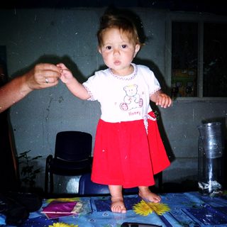 Toddler standing on table holding adult's hand.
