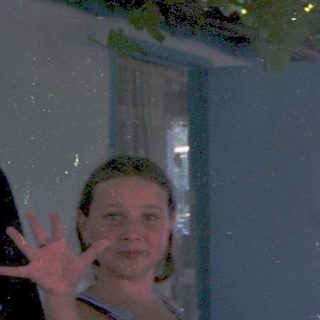 Person posing peace sign under lush green canopy.
