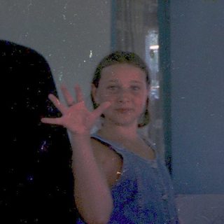 Person posing peace sign under lush green canopy.