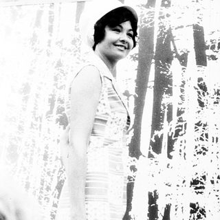Woman smiling indoors near patterned wall.