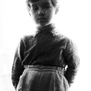 Young boy standing near a window in dimly lit room.