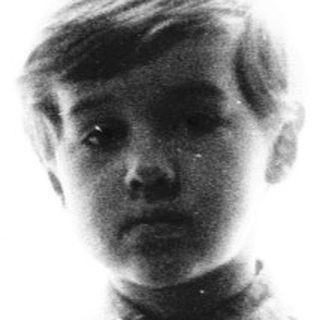 Young boy standing near a window in dimly lit room.