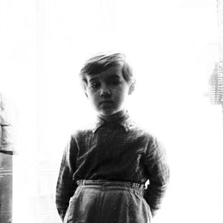 Young boy standing near a window in dimly lit room.