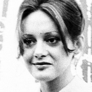 Woman in white blouse speaking at event.