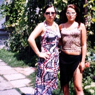 Two women posing outdoors in a lush garden.