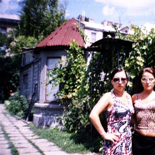 Two women posing outdoors in a lush garden.