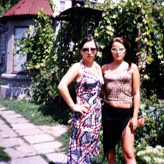 Two women posing outdoors in a lush garden.