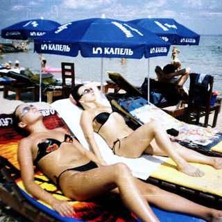 Beach scene with two women relaxing on lounge chairs.