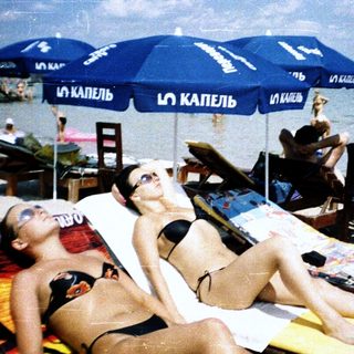 Beach scene with two women relaxing on lounge chairs.