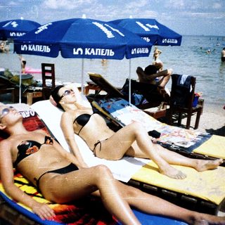 Beach scene with two women relaxing on lounge chairs.