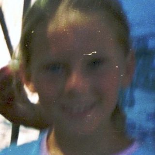 Girl smiling near water fountain on hot day.