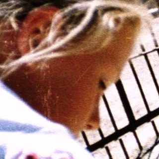 Woman feeding sheep behind metal fence.