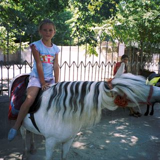 Girl riding painted pony in outdoor setting.