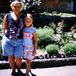 Two women posing outdoors near garden with stone structure.