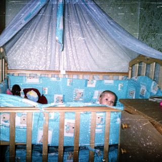 Baby sleeping in blue-themed crib with canopy.