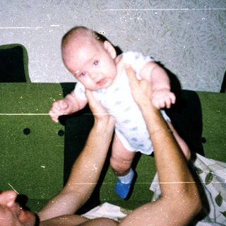 A man holding an infant above him in bed.