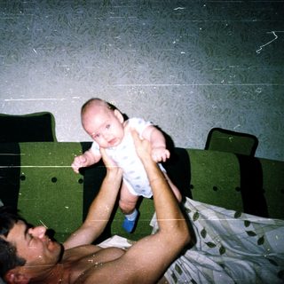 A man holding an infant above him in bed.