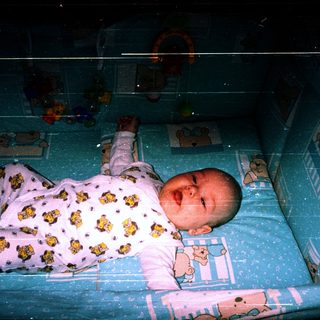 Baby sleeping in crib with teddy bear pajamas.