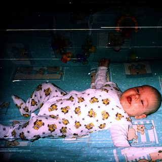 Baby sleeping in crib with teddy bear pajamas.