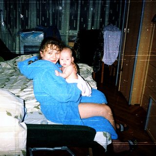 Two siblings sitting together on a bed.