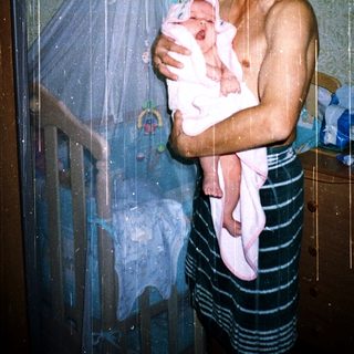 Showering man holding newborn baby.