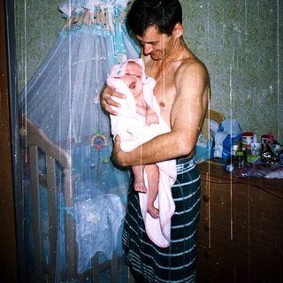 Showering man holding newborn baby.