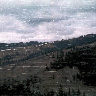 Mountainous landscape with forested slopes and snow patches.
